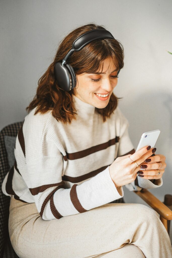 Woman wearing wireless headphones, seated indoors, browsing on smartphone.